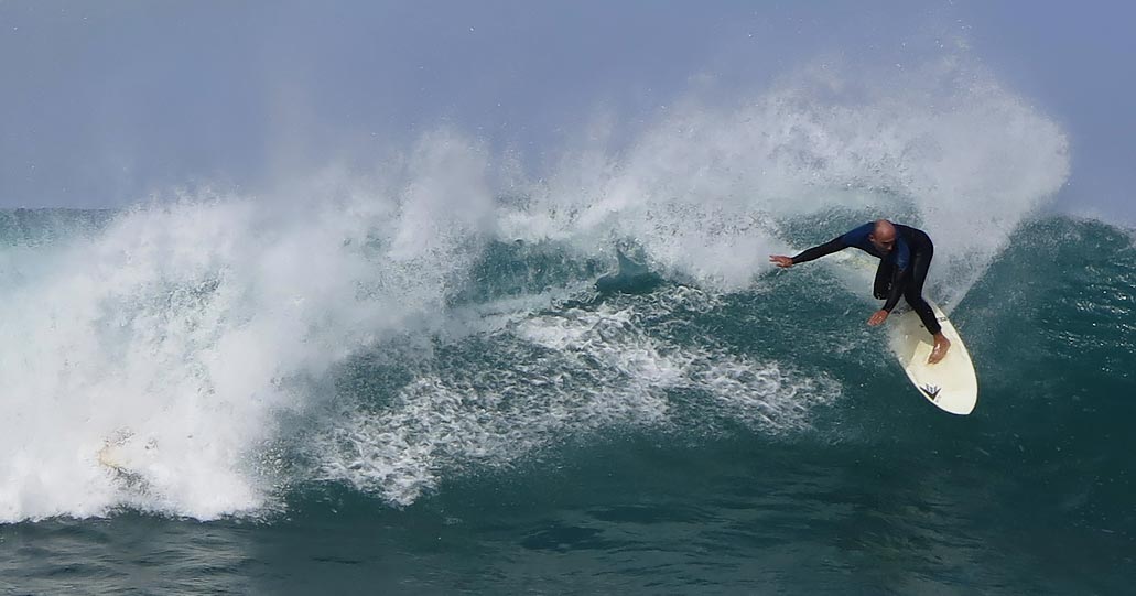 Fotografía de surfista con traje de neopreno sobre ola.